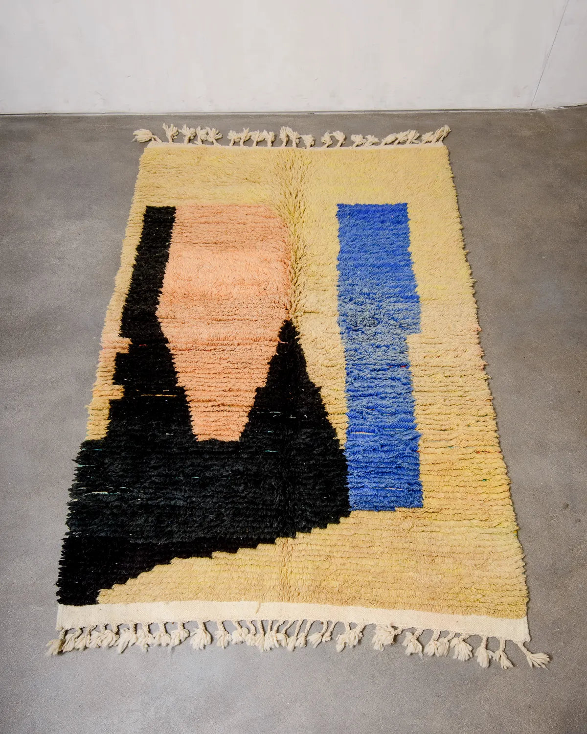 Handcrafted vintage Berber rug from Morocco in shades of yellow, apricot, blue and black, laying on concrete floor.